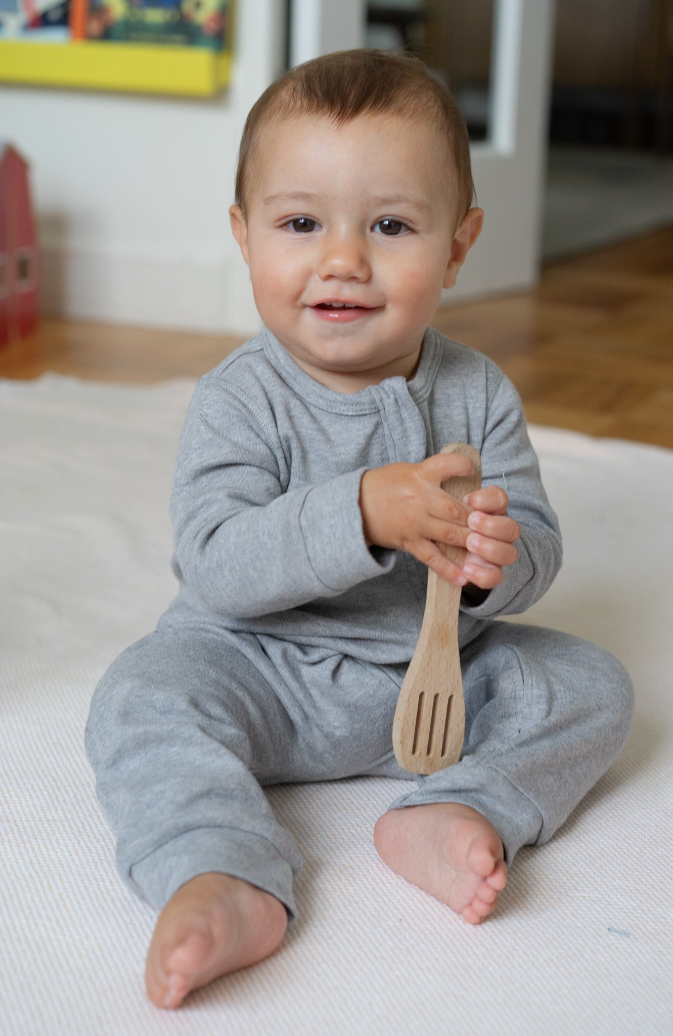 A baby sitting on the floor wearing a gray organic cotton romper with a double zipper.